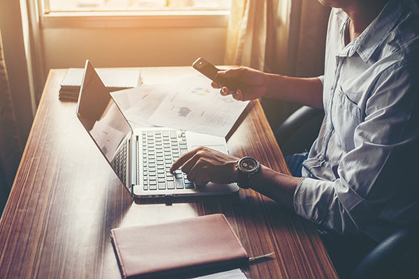 Businessman hands using cell phone with laptop at office desk. - Tax Advice For Accountants