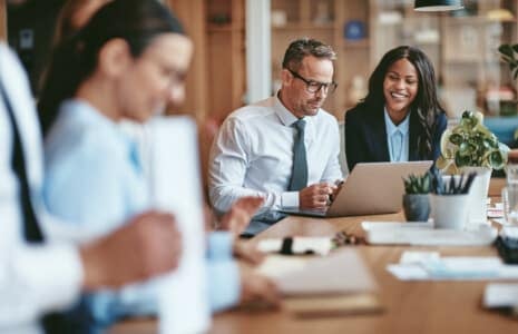 Two smiling diverse businesspeople using a laptop together at wo